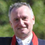 Headshot of Richard Davison, international dressage rider and coach, wearing a blue show jacket and a white shirt and tie.
