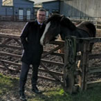World Horse Welfare Director of Fundraising patting bay pony over wooden gate