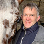 The headshot of Malcolm Morley, World Horse Welfare's Director of UK, wearing a blue jacket and standing next to a horse in a stable.